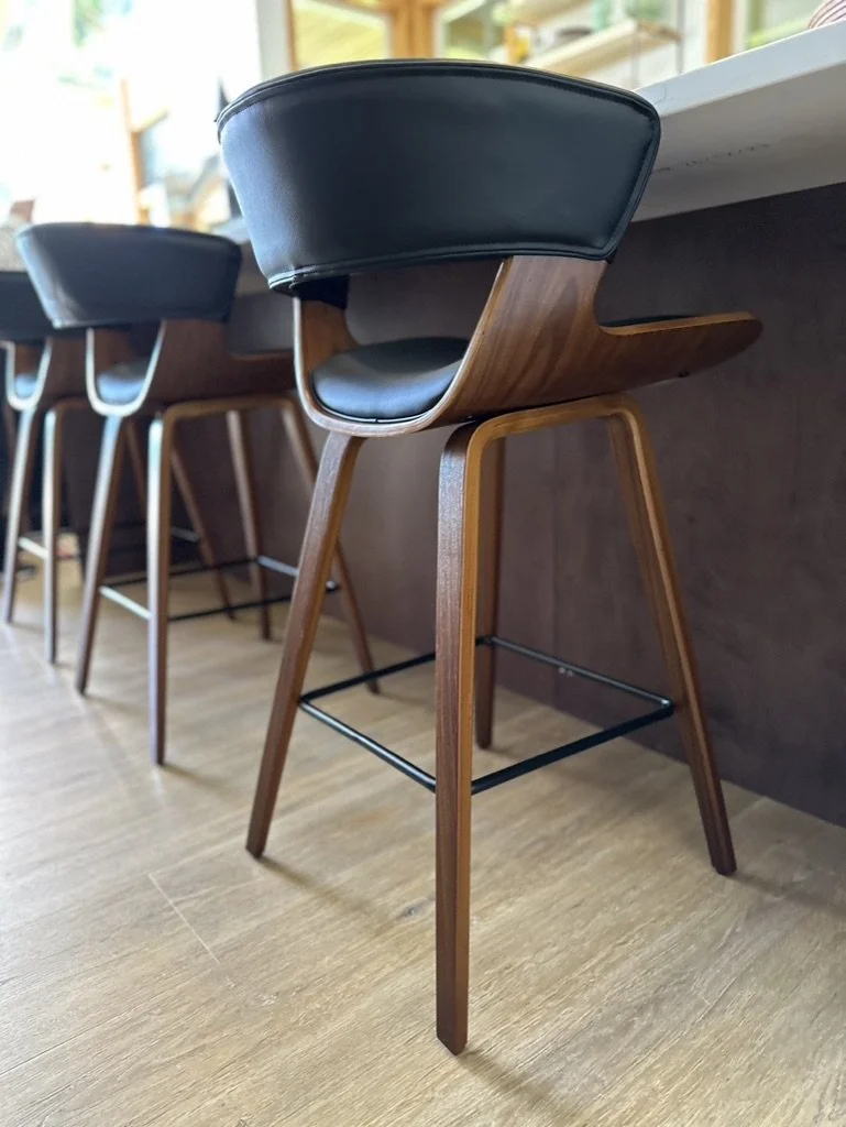 Modern wooden barstools with black cushioning at a countertop.