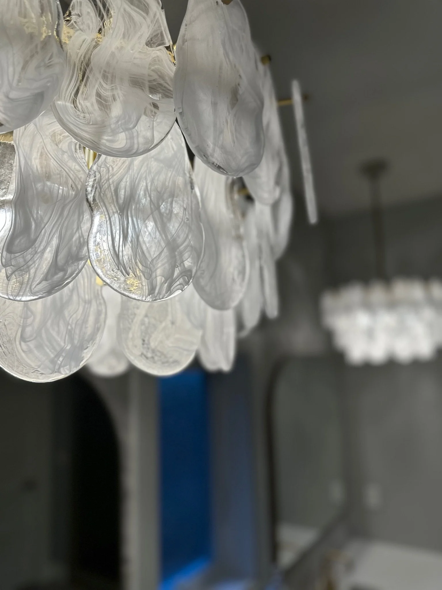 Close-up of artistic, translucent, white glass pendants with swirling patterns, part of a ceiling light fixture.