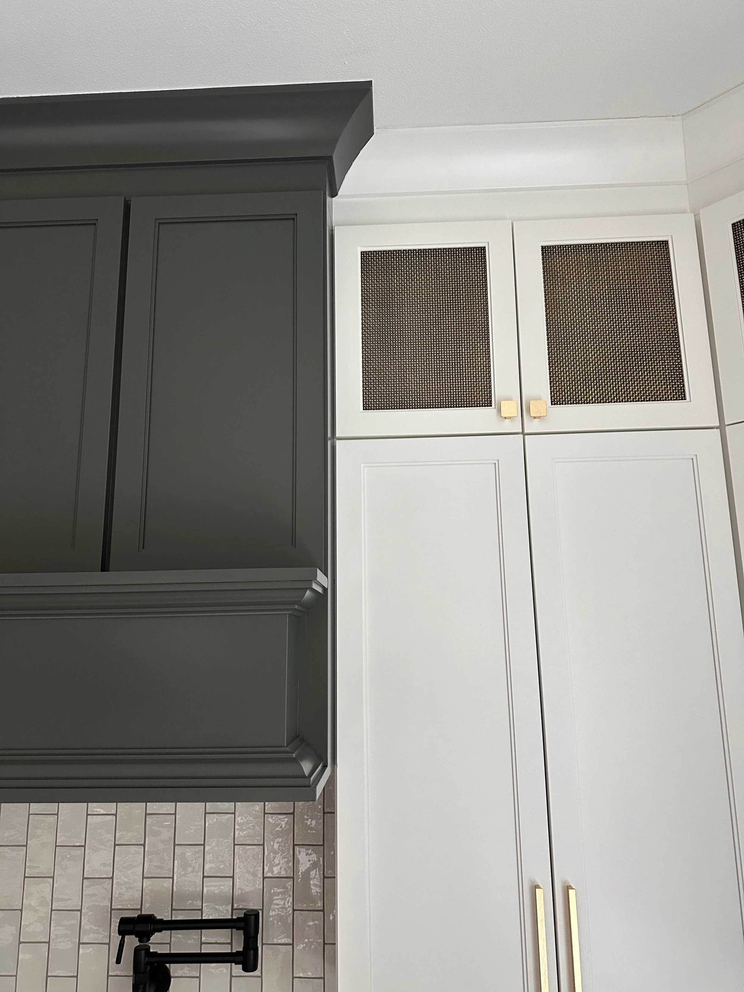 Modern kitchen with dark green and white cabinets, gold hardware, tile backsplash, and a wall-mounted pot filler.