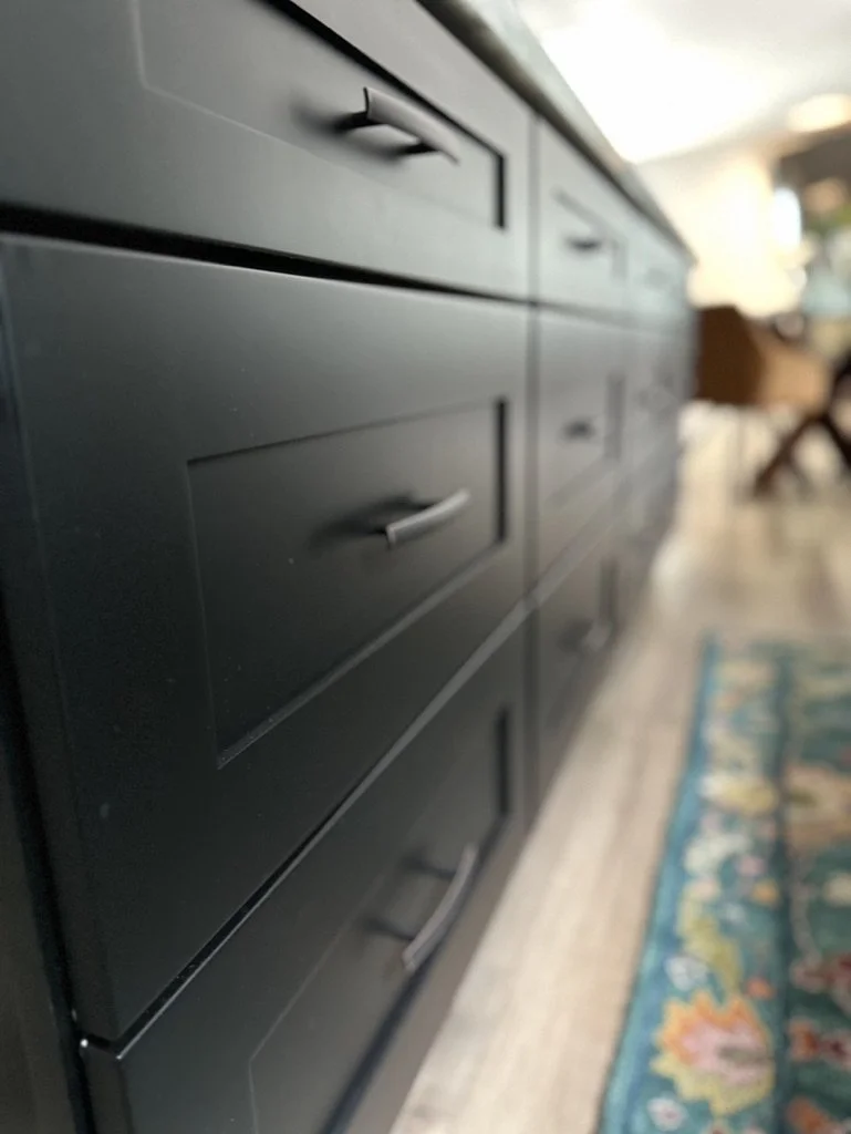 Close-up of black kitchen cabinets with handles, next to a patterned rug.