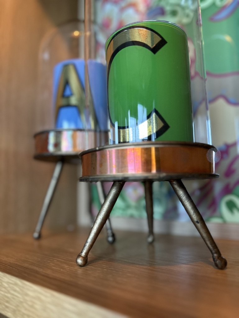 Close-up of decorative letters "A" and "C" inside glass domes on tripod stands.