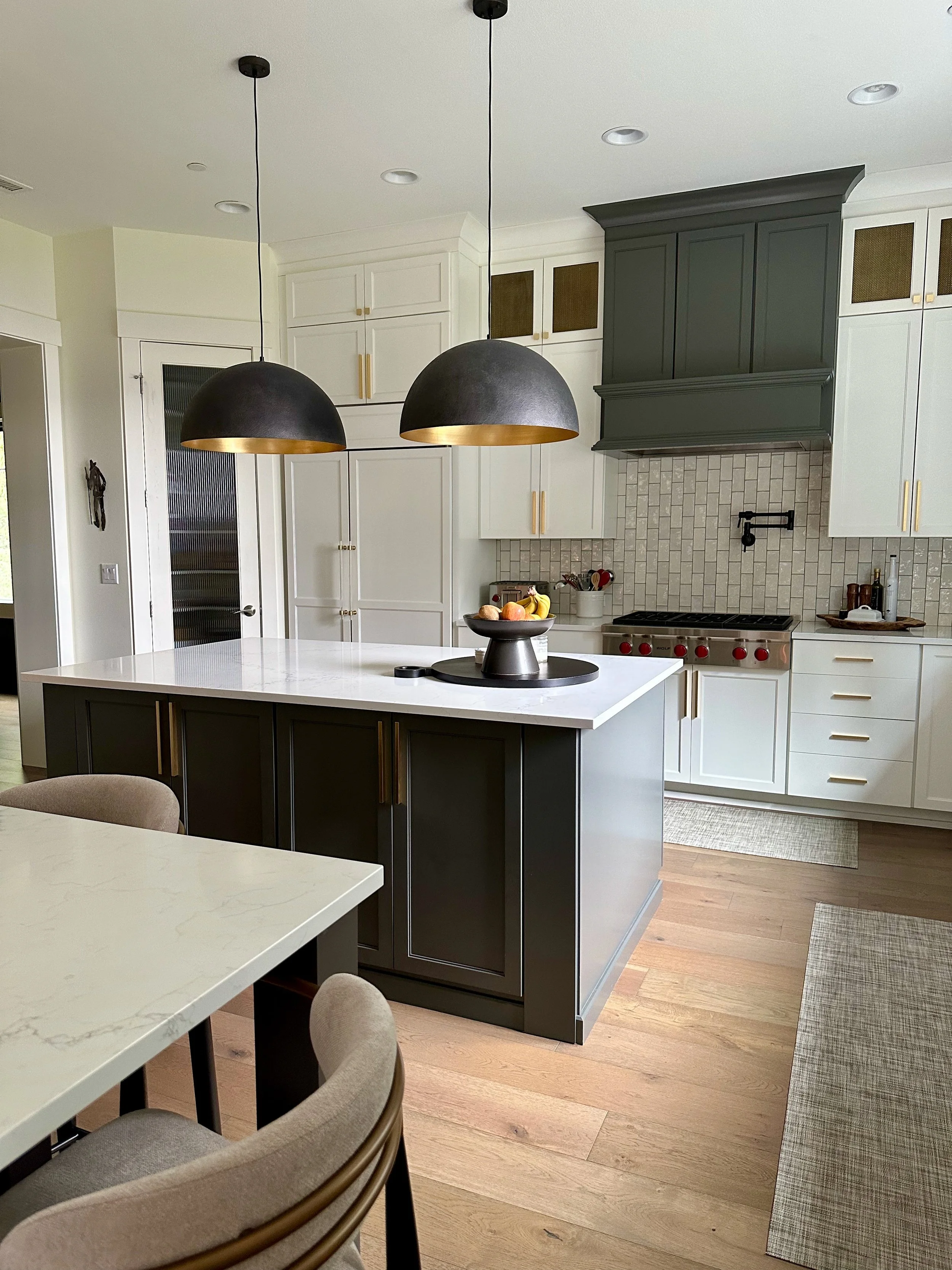 Modern kitchen interior with white cabinets, dark gray island, pendant lights, and stainless steel appliances.