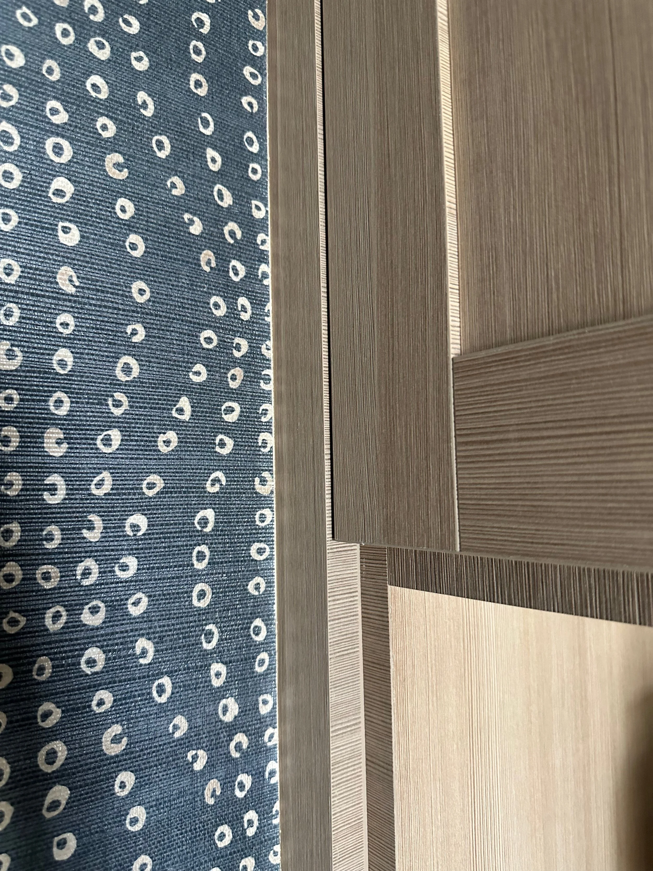Close-up of a patterned blue fabric with white circular designs next to several panels with a wood grain texture.