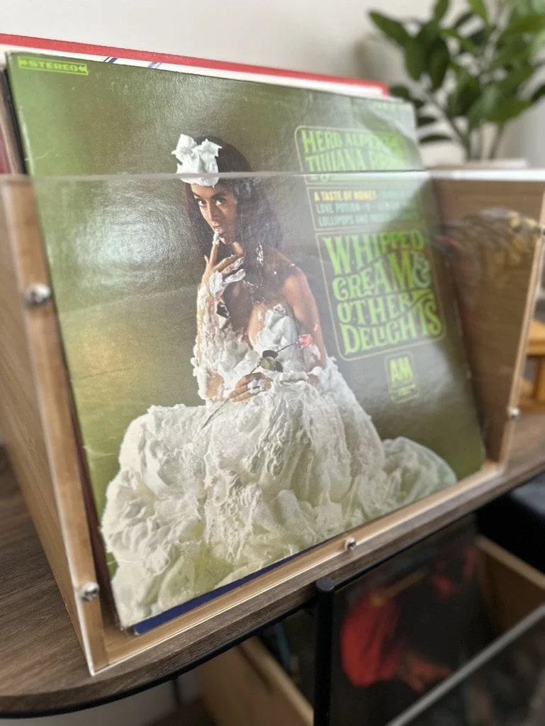 Vinyl record of Herb Alpert's "Whipped Cream & Other Delights" in a wooden record box on a table.