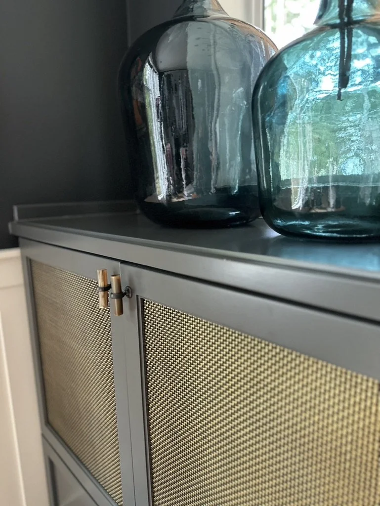 Two large blue glass bottles on a gray cabinet with textured doors.