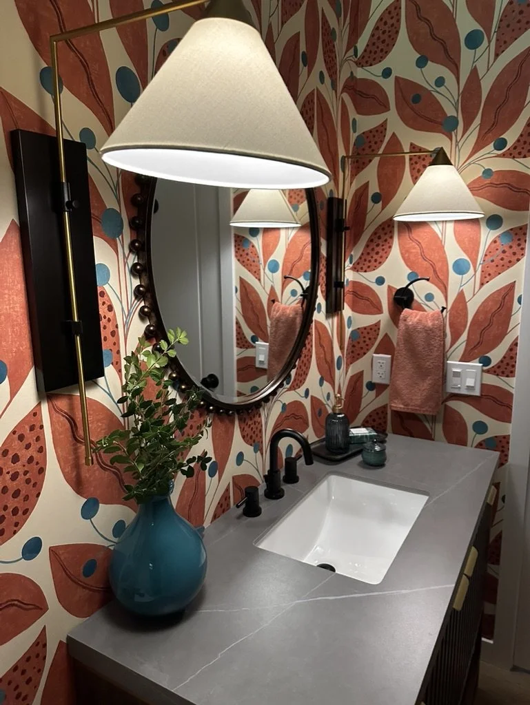 Bathroom interior with a modern sink, floral wallpaper, round mirror, and black fixtures.