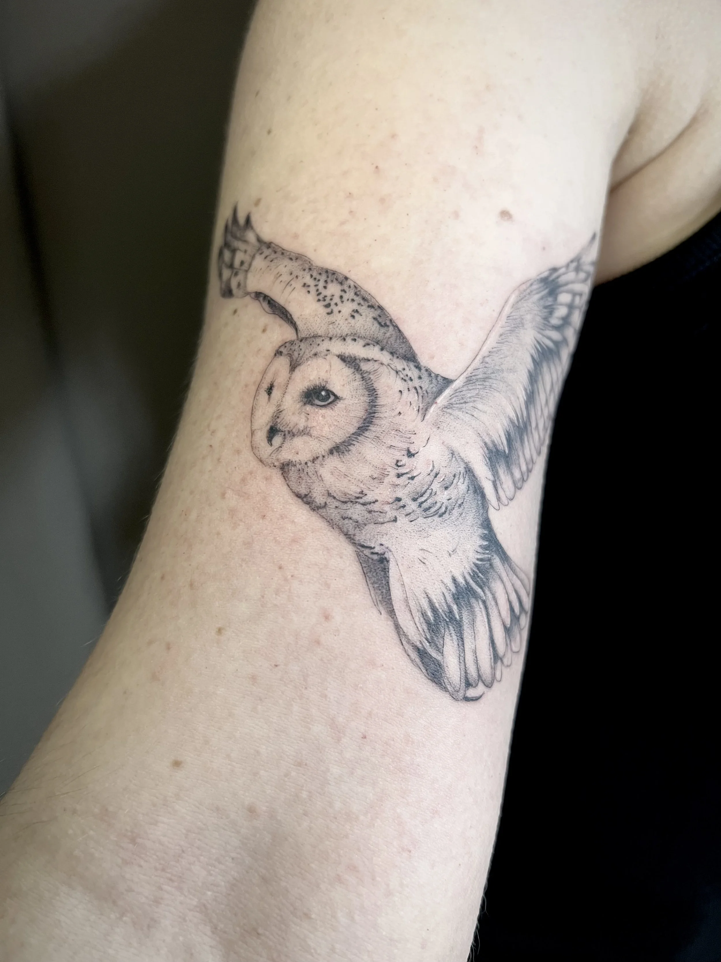 Tatouage d'une chouette en vol, dessinée en noir et blanc, avec une transformation artistique de la tête de la chouette en visage d'humain