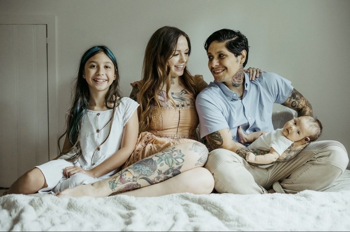 Smiling family on bed with baby and child, capturing love, unity, and joy of new parenthood