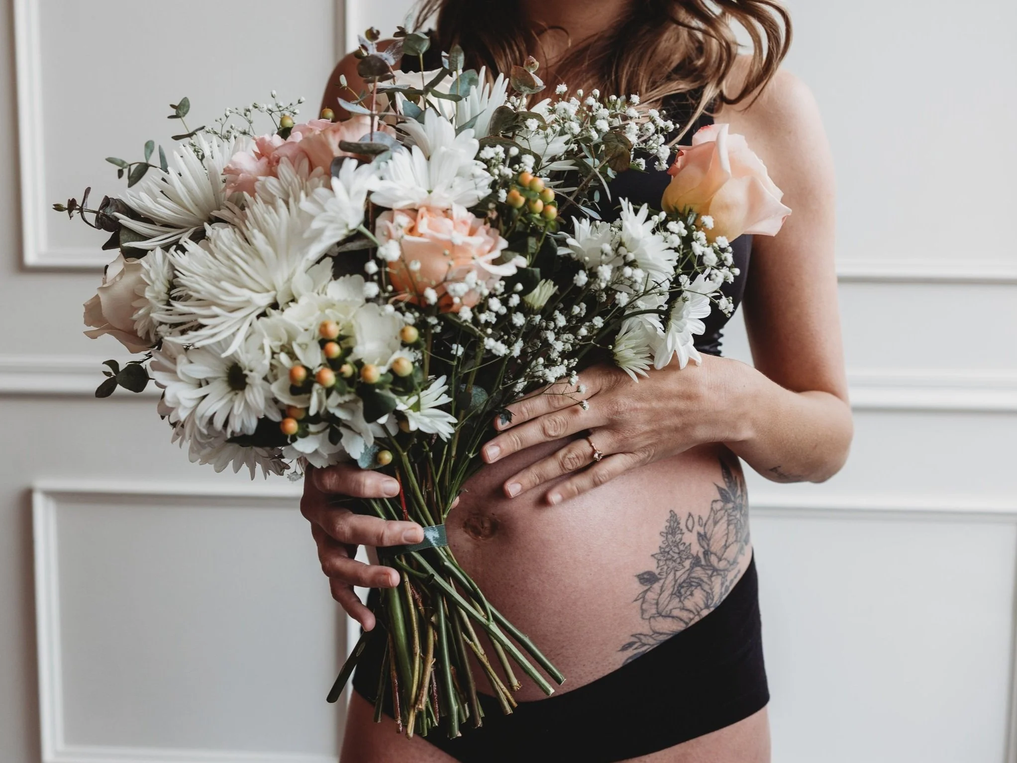 Pregnant woman holding bouquet near belly with floral tattoo, celebrating motherhood and holistic pregnancy