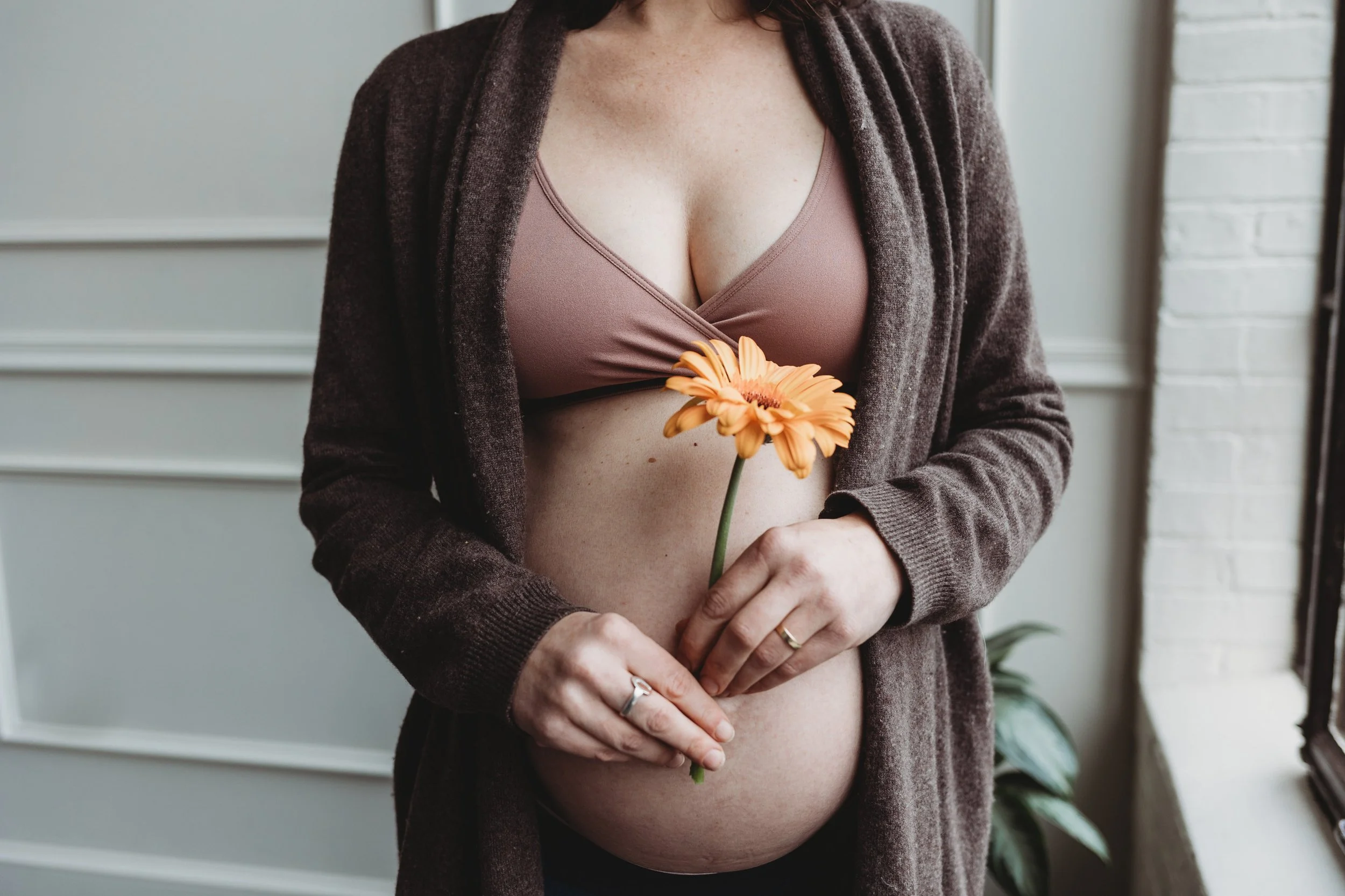 Pregnant woman holding orange flower on bare belly, symbolizing life and holistic pregnancy in a serene setting