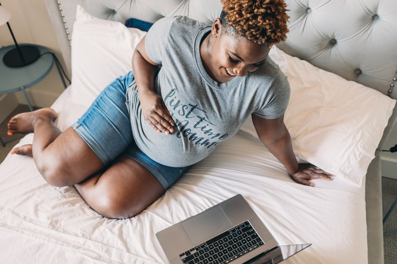 Smiling pregnant woman on bed with laptop, enjoying online classes for first time mommy and expectant parents
