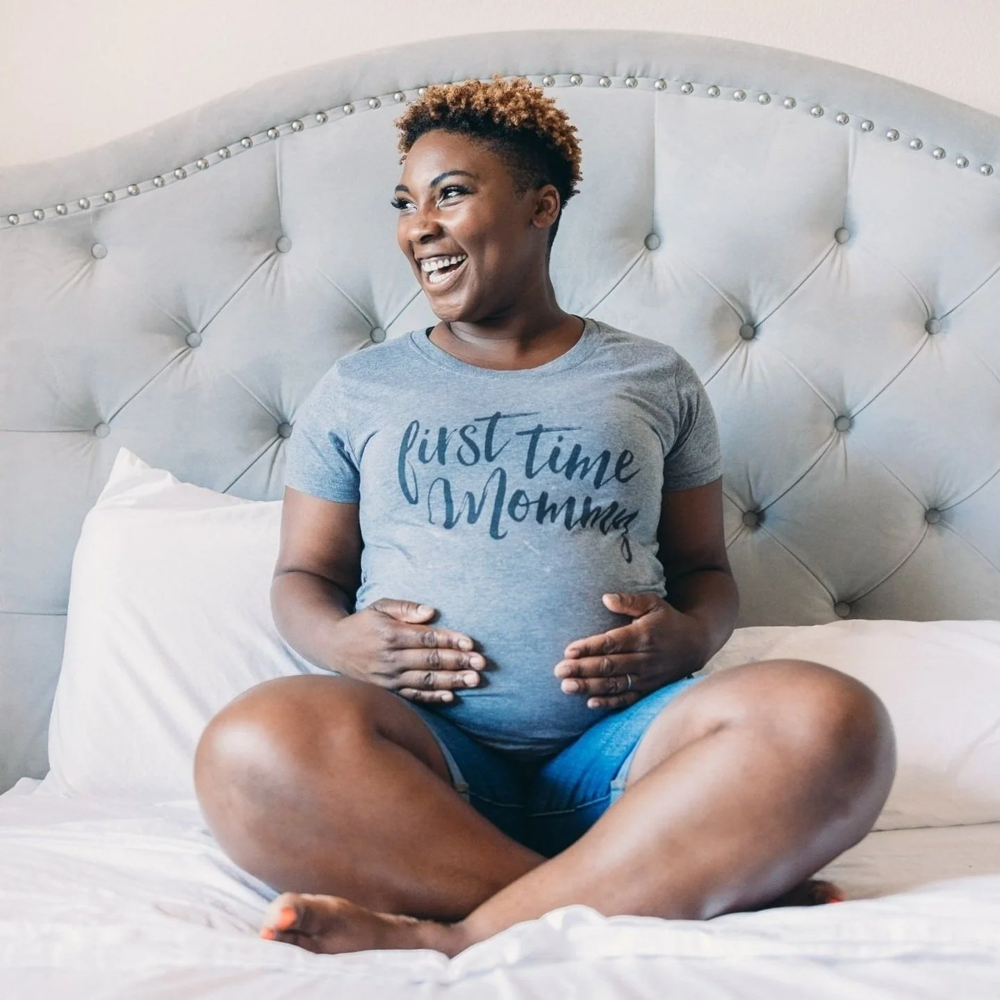 Smiling pregnant woman on bed holding belly, celebrating excitement of first time mommy and expectant parents