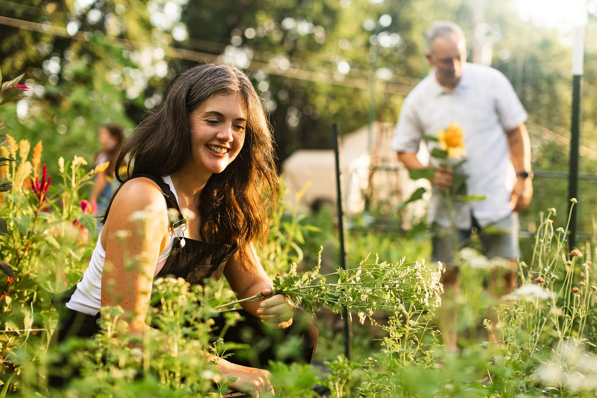 Grace Grace Gardens photoshoot: smiling woman among flowering plants with a gardener working behind her