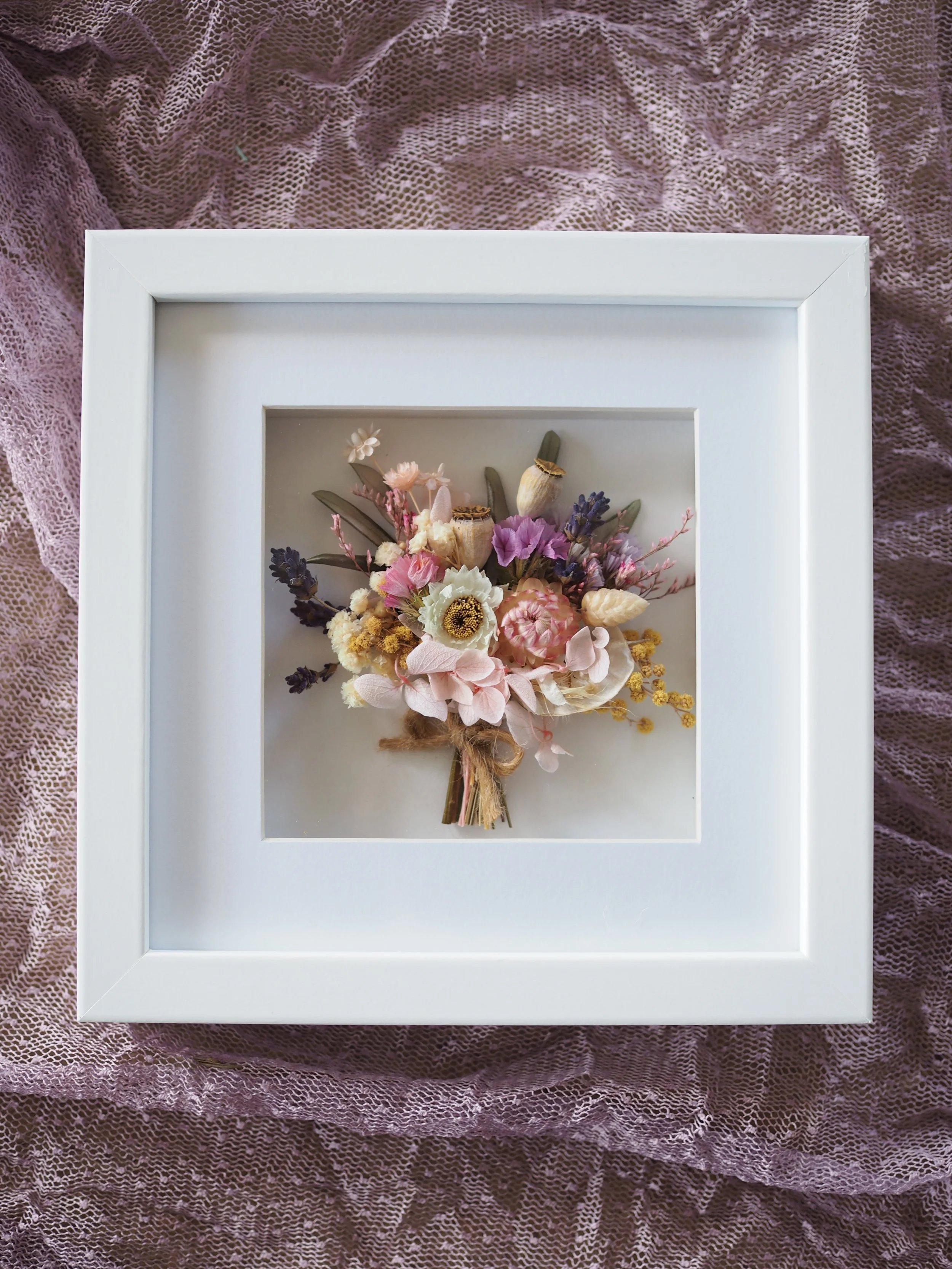 The exquisite Little Petals Frame is a darling design showcasing a dainty bouquet crafted from dried and preserved florals on a crisp white backdrop