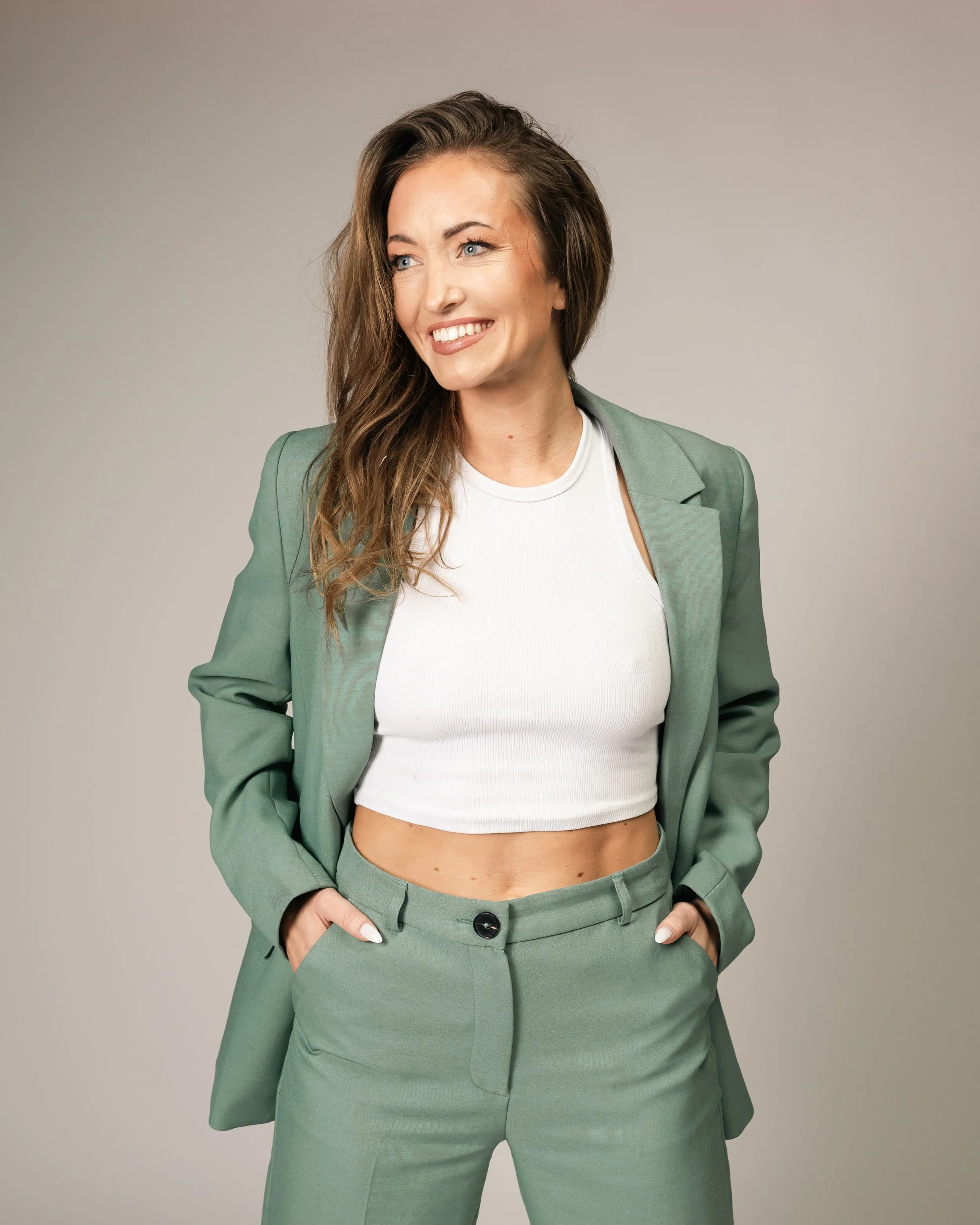 Kvinne i grønn dresser med hvit crop topper, smilende og med hendene i lommene.