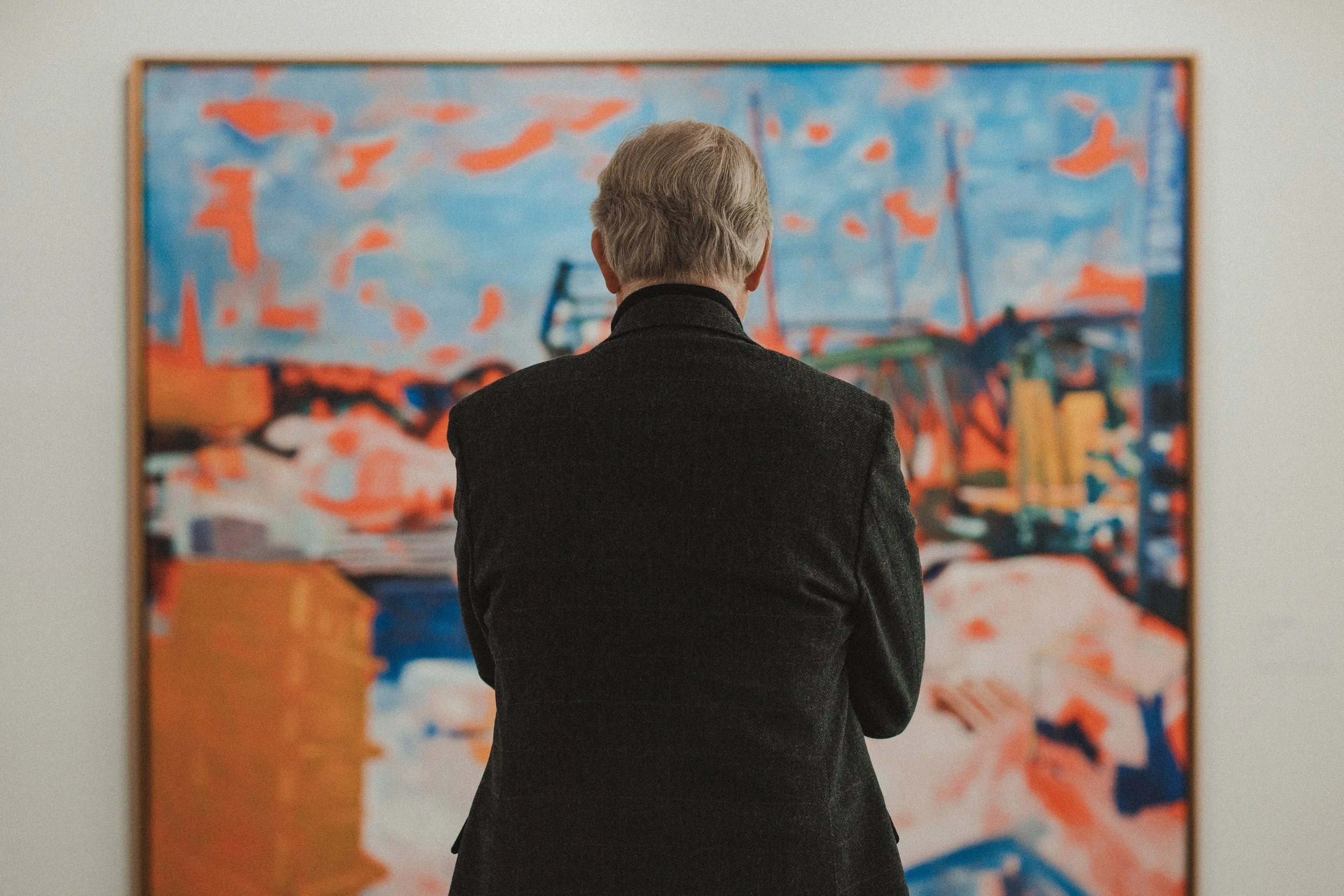 En eldre mann sett bakfra som ser på et abstrakt maleri i et kunstgalleri.
