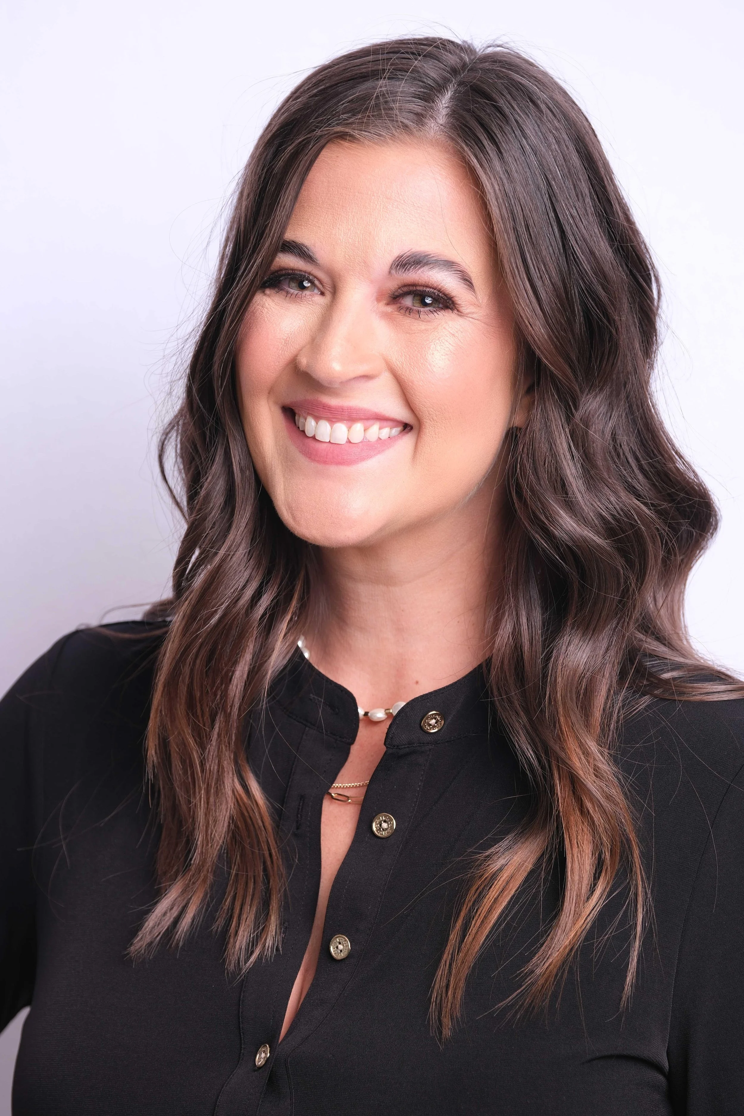 A woman with shoulder-length brown hair and a black top, smiling at the camera, against a plain light background.