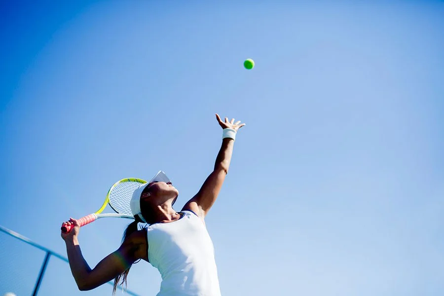 Female tennis player serving under a clear blue sky during a summer tennis match