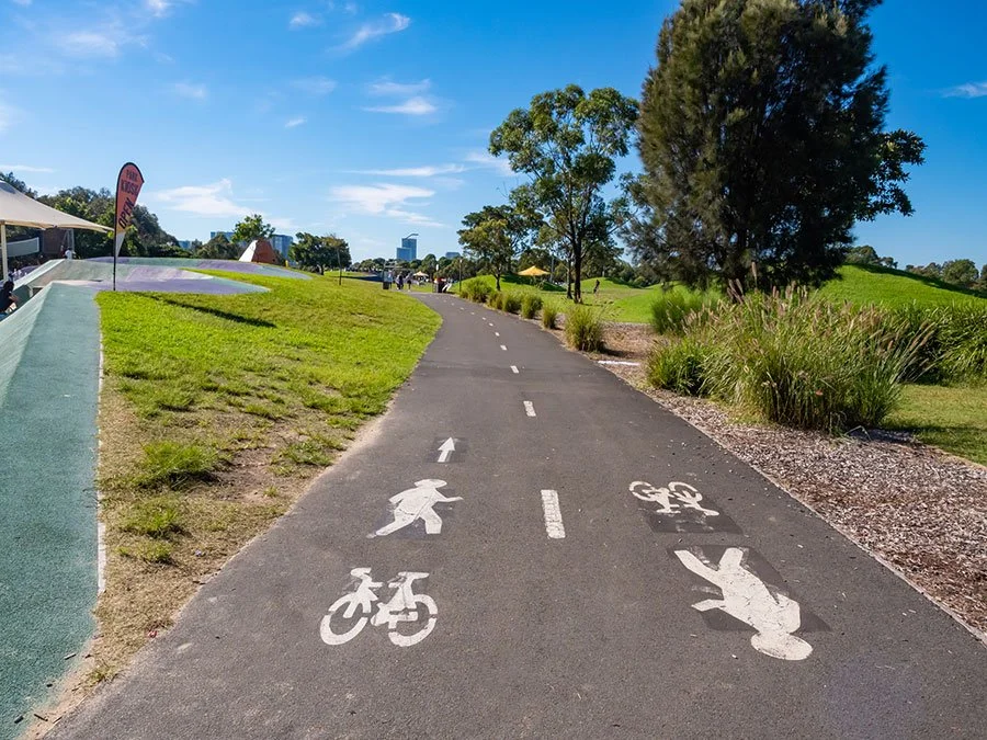 Cyclists and walkers using a shared bike path through a green urban park in Sydney