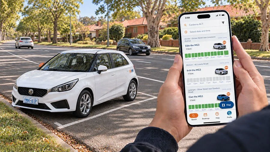 Hands holding a smartphone showing the GoGet app's list of available cars in Canberra suburbs, with a white GoGet hatchback parked on a leafy suburban street behind.