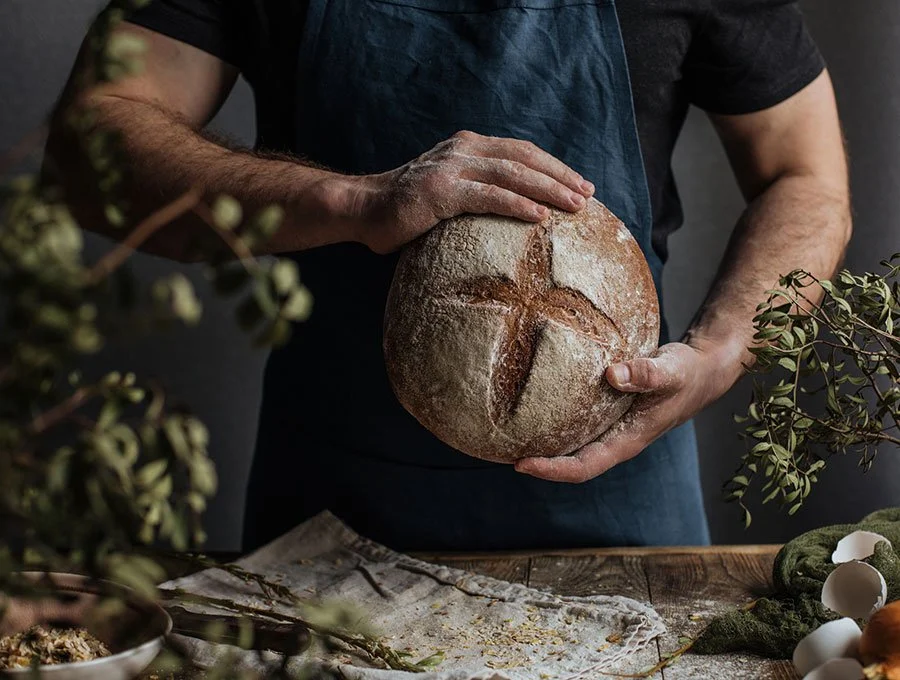 Artisan baker holding a freshly baked sourdough loaf, showcasing the crusty, rustic texture typical of Melbourne’s best bakeries.