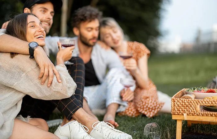 Group of friends gathered around a picnic spread with wine and food, enjoying a relaxed outdoor afternoon at a regional food festival