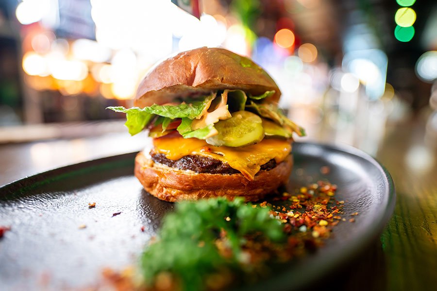 Loaded gourmet cheeseburger with beef patty, melted cheese, pickles, lettuce, and sesame bun — perfect food truck-style street food