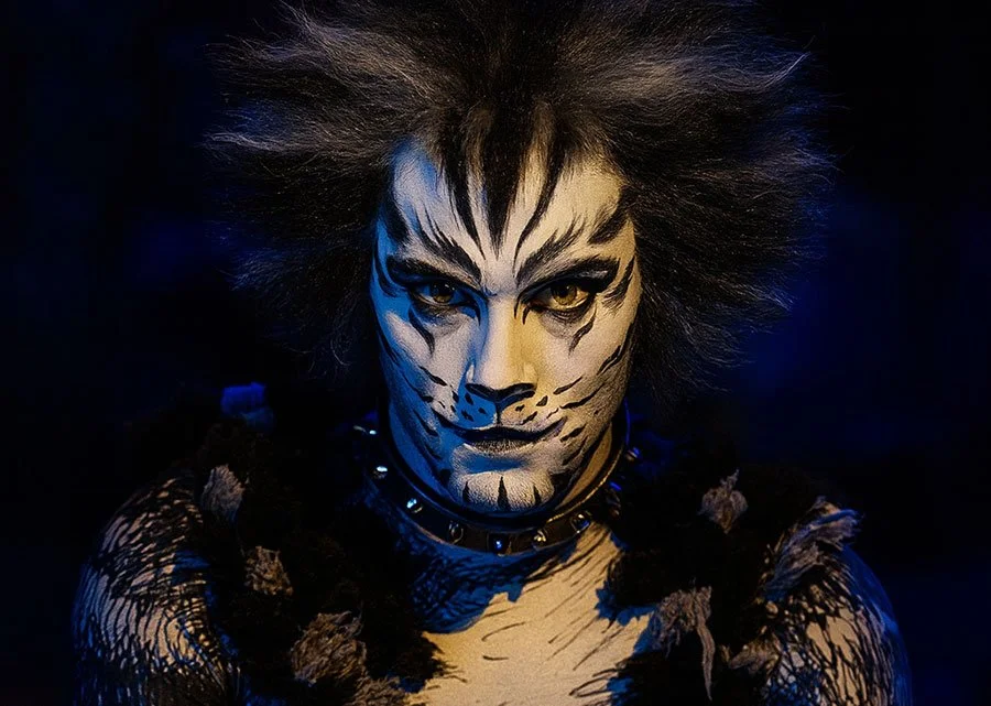 Performer in dramatic cat stage makeup and costume under blue stage lighting in a musical theatre production