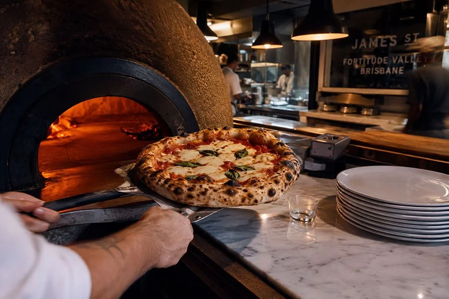 A margherita pizza coming out of a woodfired oven on a metal peel at an Italian restaurant on James Street, Fortitude Valley, Brisbane.