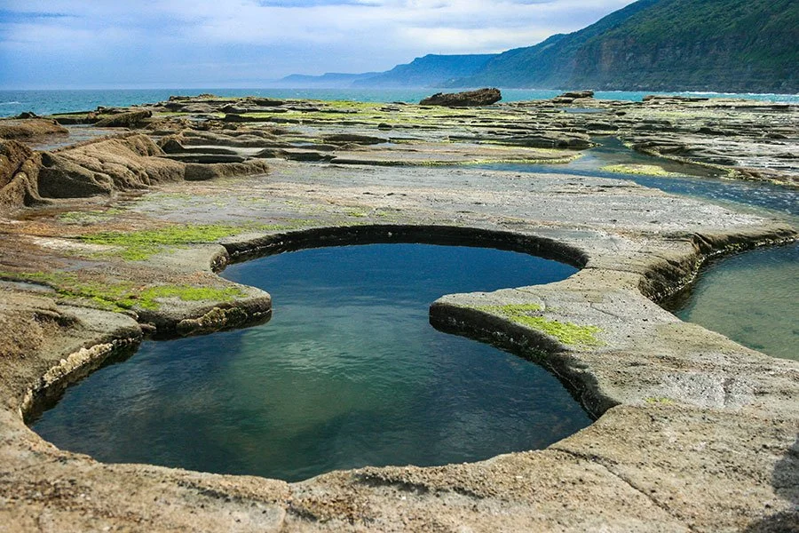Aerial view of a natural figure-8 shaped rock pool carved into a coastal shelf with clear water and ocean views near Sydney