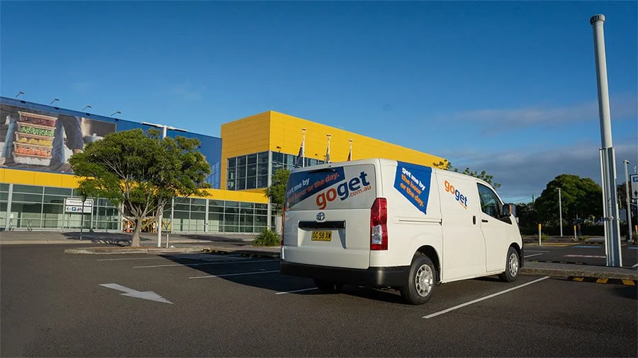 White GoGet van parked in a wide retail IKEA car park outside a large blue and yellow IKEA warehouse store under a clear sky.