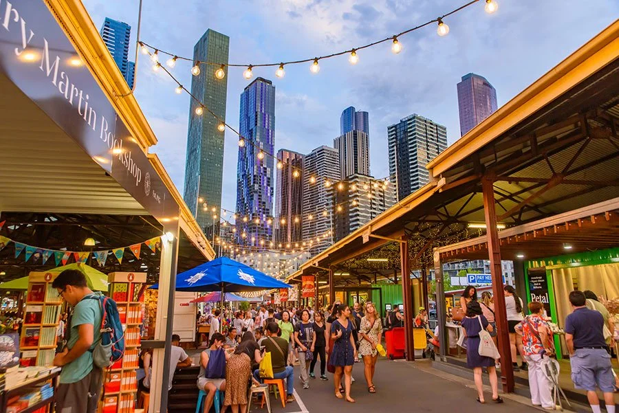 Queen Victoria Market in Melbourne lit up at night with food stalls and city skyline in the background