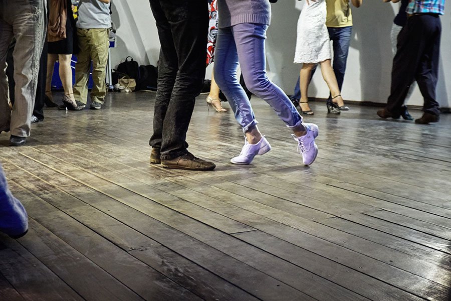 Close-up of people's feet and legs dancing together on a timber floor at a casual community dance event