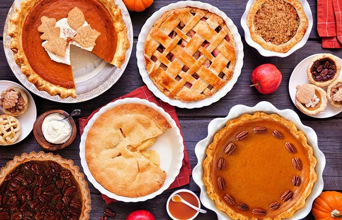 Selection of freshly baked autumn pies with pumpkin, apple and pecan on a rustic wooden table, showcasing seasonal harvest flavours