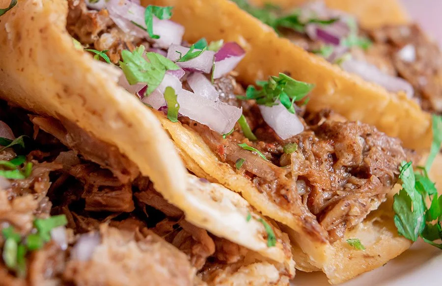 Close-up of crispy birria tacos topped with onion and coriander — a popular Mexican street food made with slow-cooked beef