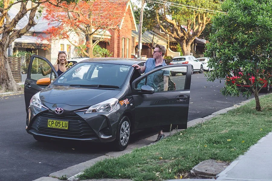 Two friends getting into a GoGet car on a quiet Sydney street, ready to explore local food trucks and street eats