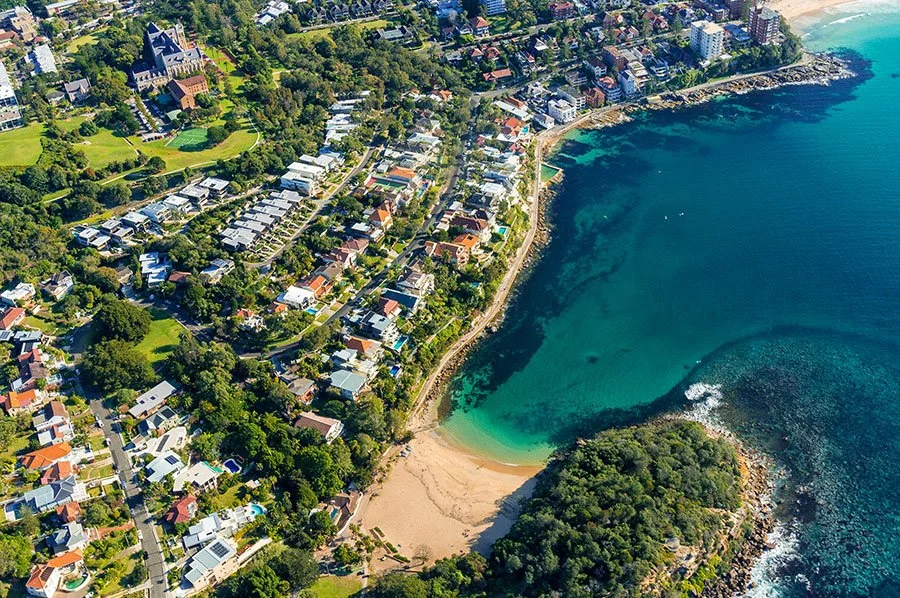 Aerial view of a Sydney coastal bay with cliffs, bushland, and clear water near a popular walking trail