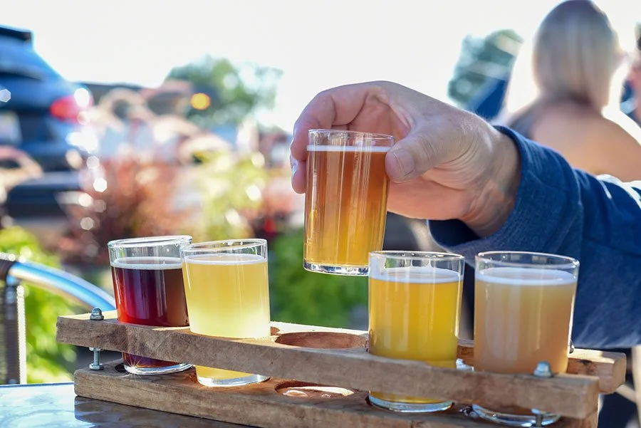 Hands sampling tasting flight of craft drinks at outdoor table distillery cellar door