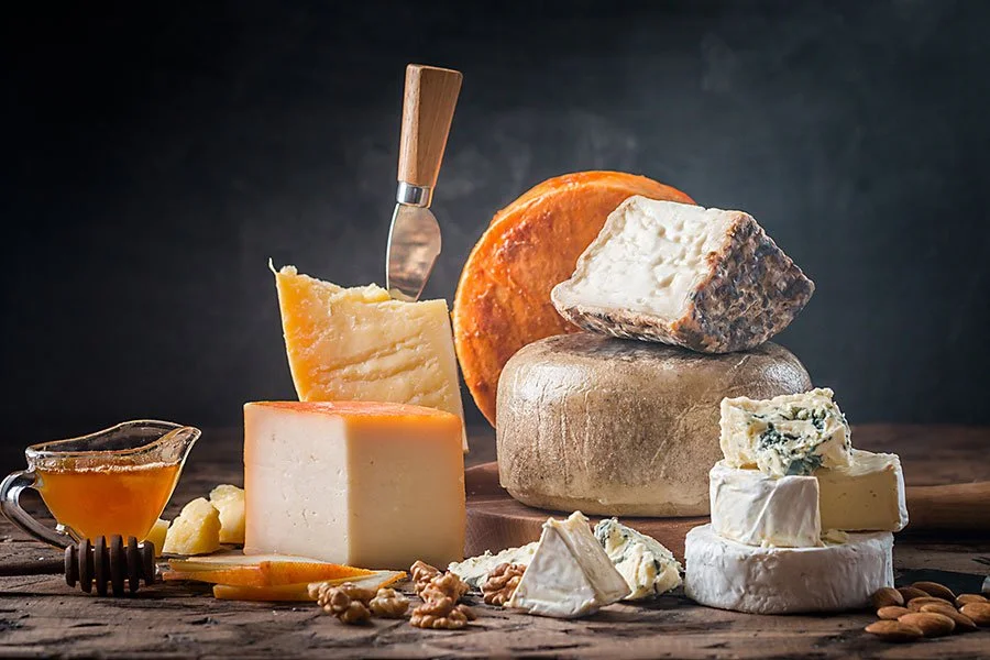 Assorted artisan cheeses including soft cheese, aged varieties and fresh curd displayed on wooden board