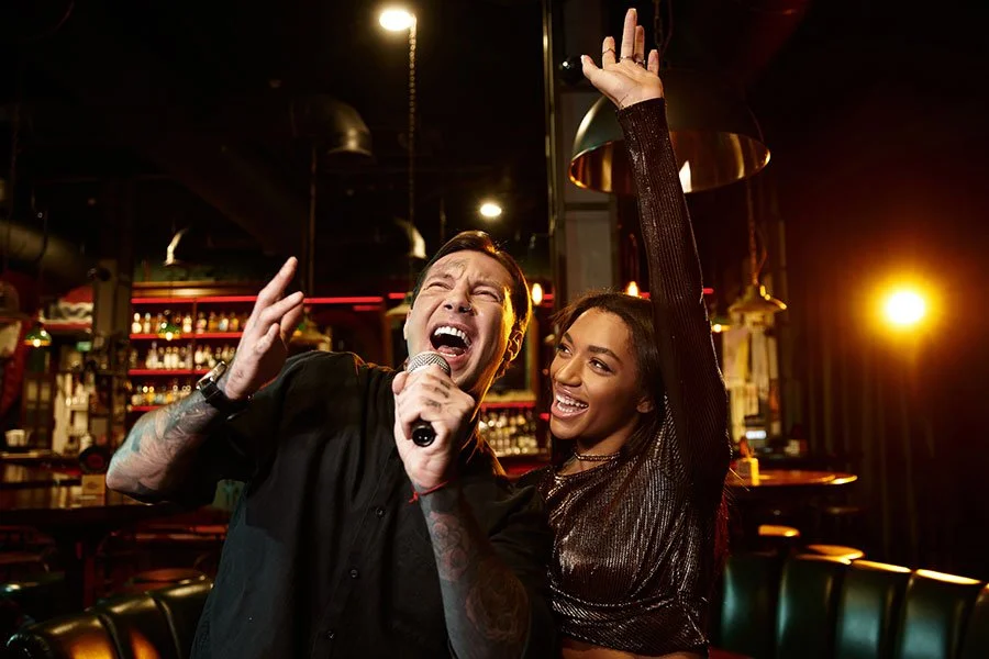 Two friends singing enthusiastically with a microphone in a dimly lit karaoke bar at night