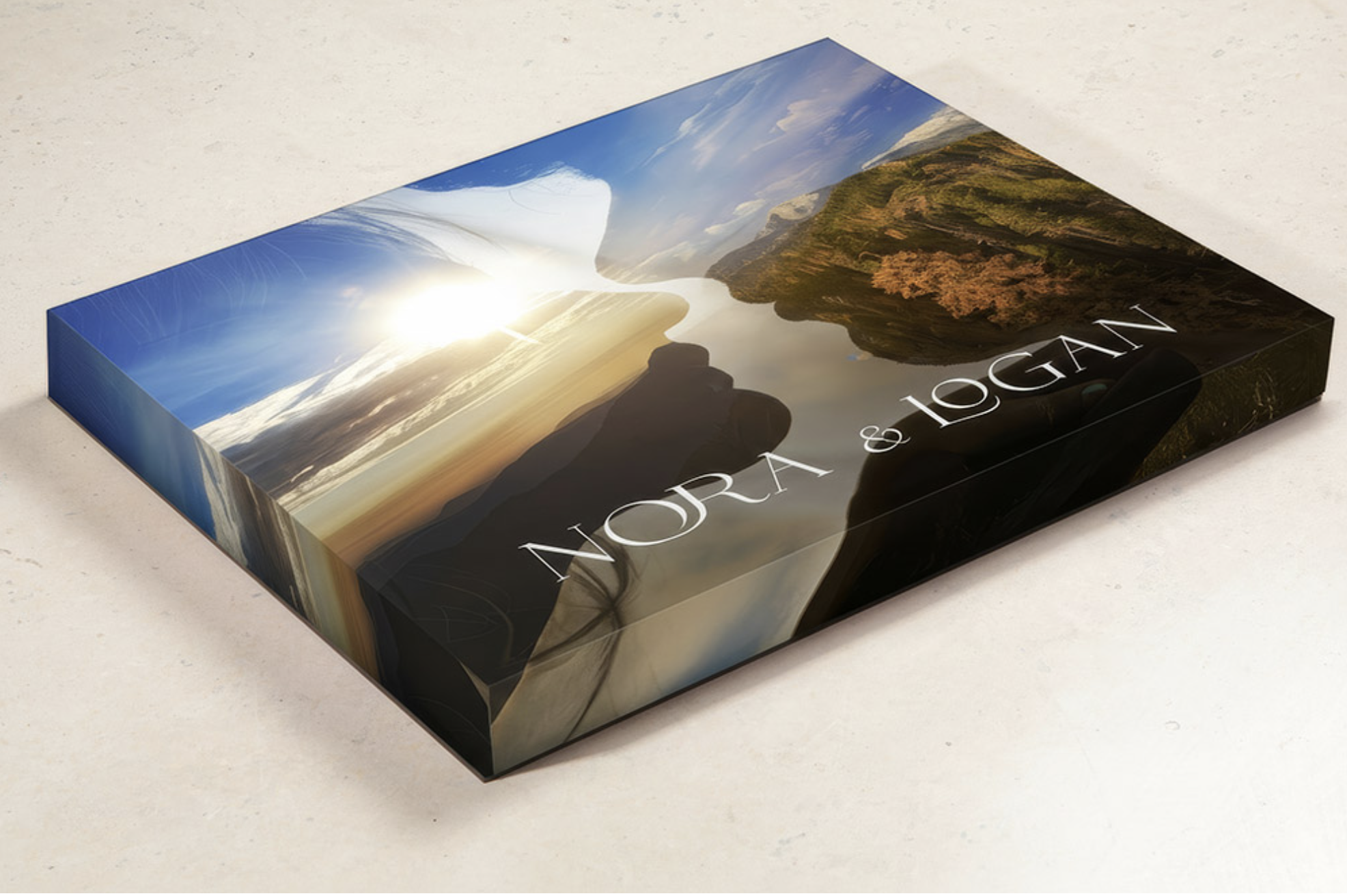A rectangular book with a cover featuring a scenic landscape of mountains, a river, trees, and sky during sunset, with the text 'WORAN & LOGAN' printed on it.