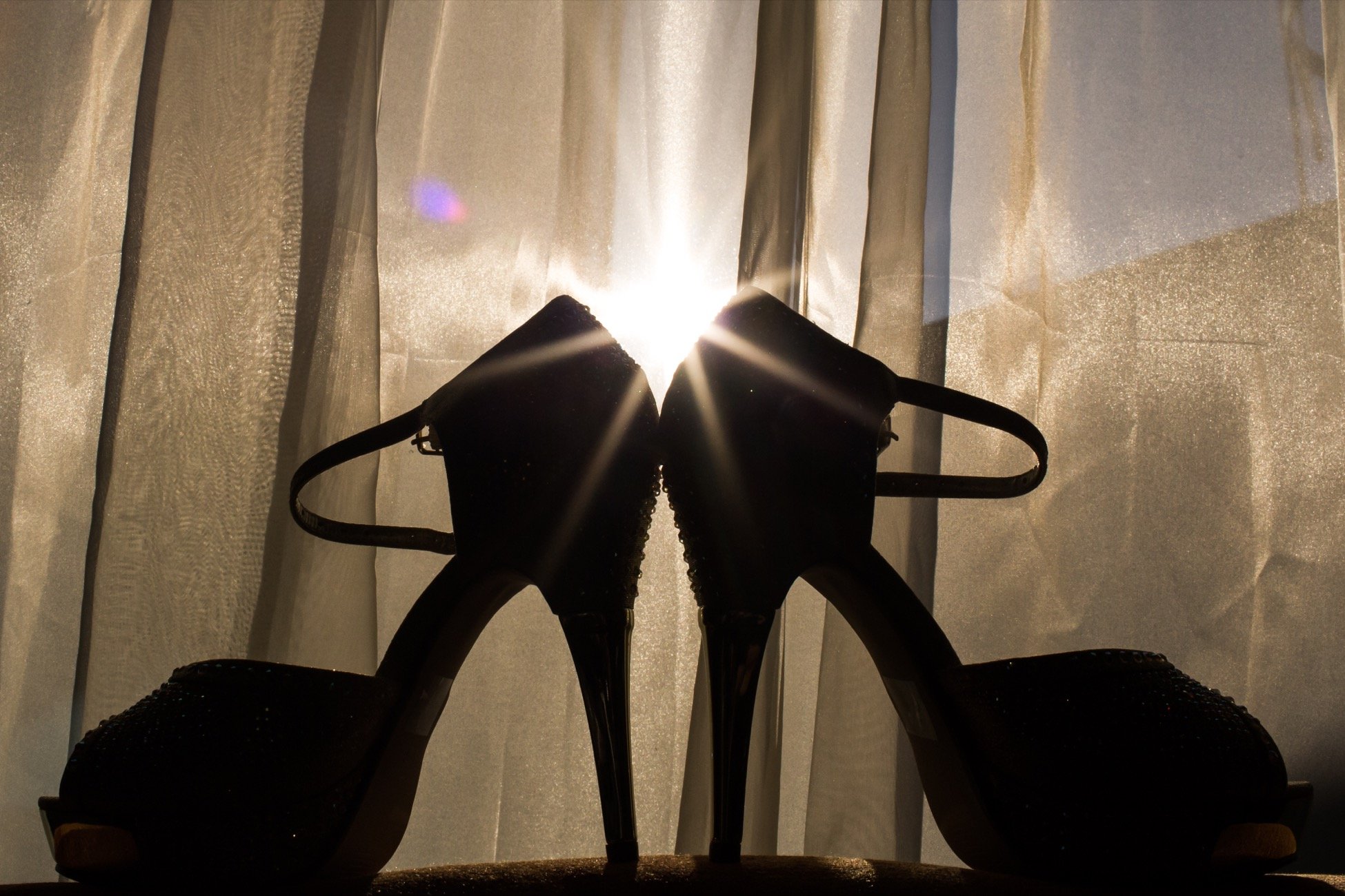 A pair of black athletic shoes on a surface with sunlight shining through a curtain in the background.