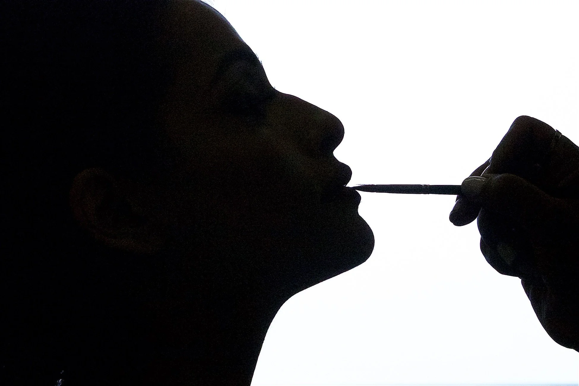 Silhouette of a person with their head tilted back, holding a nail polish brush near their lips against a white background.