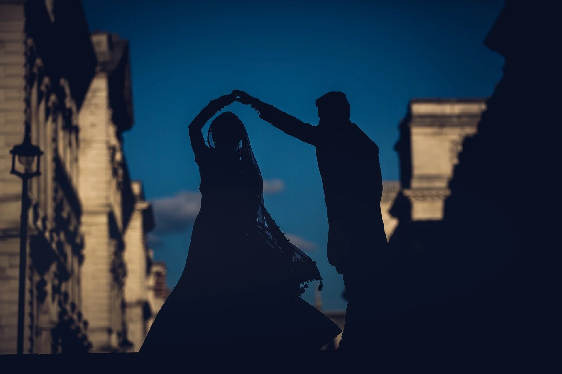 Silhouettes of a couple dancing on a city street at dusk with historic buildings in the background.