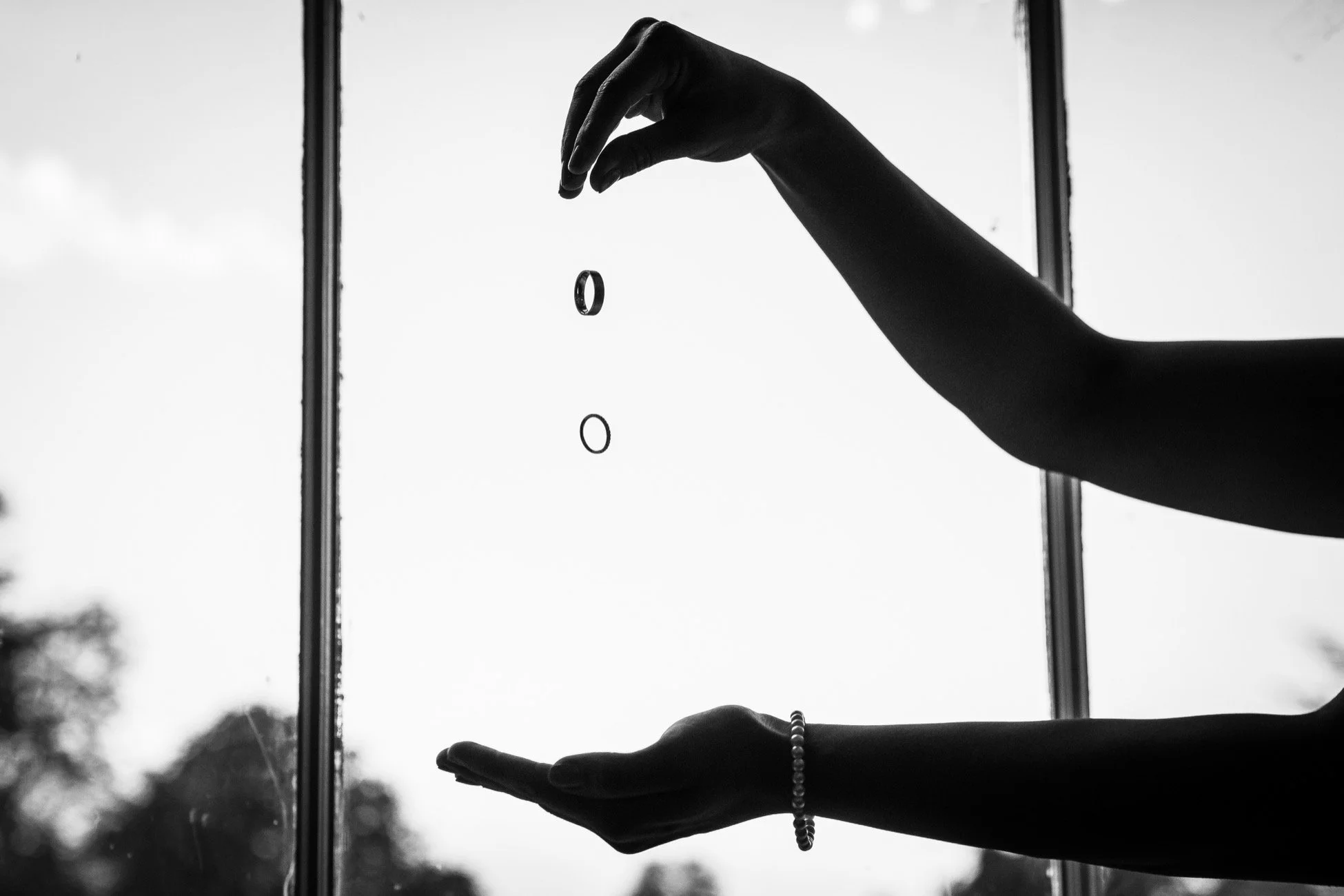 Black and white photo of a person's hands holding small rings, with a window in the background.