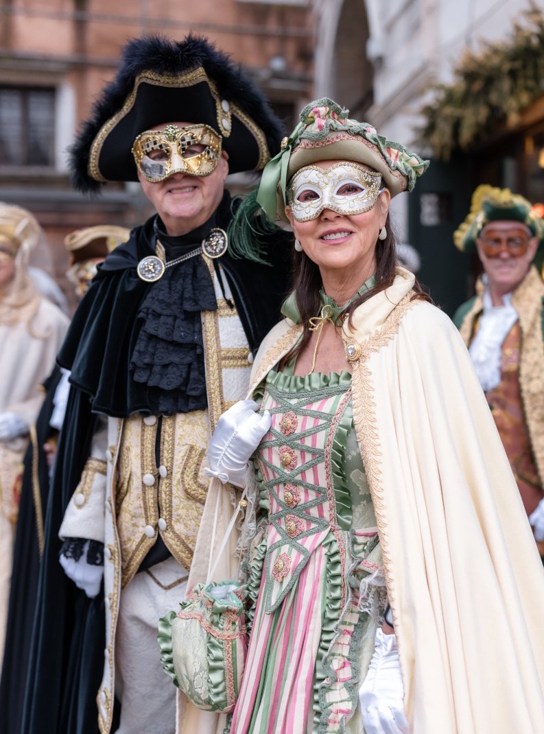 People dressed in elaborate costumes and masks participating in a parade on their way to Ballo dalle Rose.