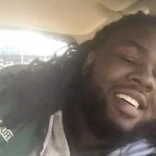 Close-up of a smiling man with long hair, sitting in a vehicle.