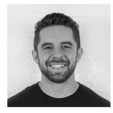 Portrait of a man with short dark hair, a beard, and a mustache, smiling, wearing a black shirt.