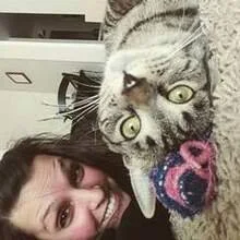 A young woman with dark hair and a gray tabby cat lying on a knitted blanket.