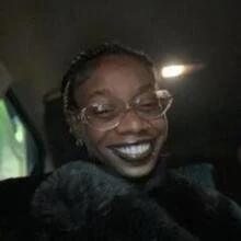 A woman with glasses smiling inside a car at night.